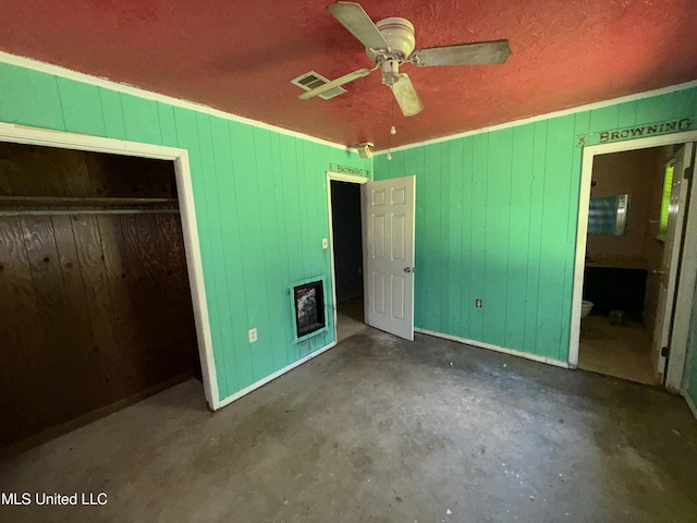 unfurnished bedroom featuring unfinished concrete flooring, wood walls, a closet, connected bathroom, and a ceiling fan