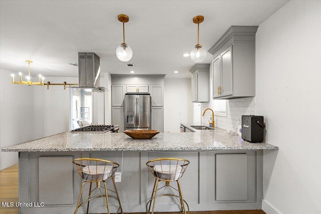 kitchen featuring hanging light fixtures, range hood, kitchen peninsula, decorative backsplash, and appliances with stainless steel finishes