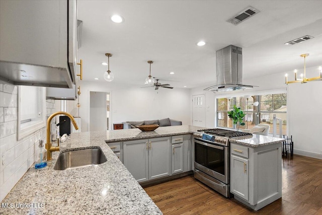 kitchen with ceiling fan with notable chandelier, island range hood, sink, stainless steel gas stove, and hanging light fixtures