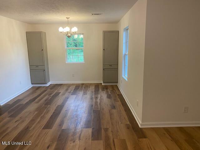 unfurnished dining area with baseboards, visible vents, an inviting chandelier, and dark wood-type flooring