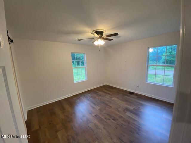 empty room featuring baseboards, ceiling fan, and dark wood-type flooring