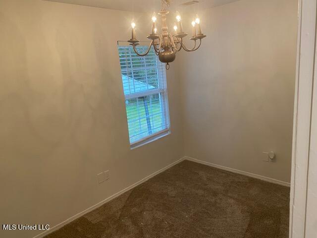 spare room with an inviting chandelier, dark carpet, and baseboards