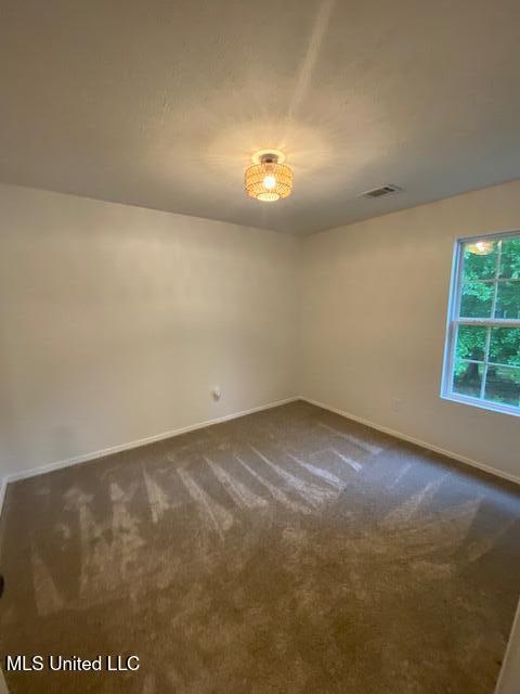 empty room featuring baseboards, dark colored carpet, and visible vents