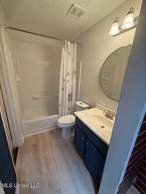full bath with a textured ceiling, visible vents, shower / bathtub combination with curtain, wood finished floors, and vanity