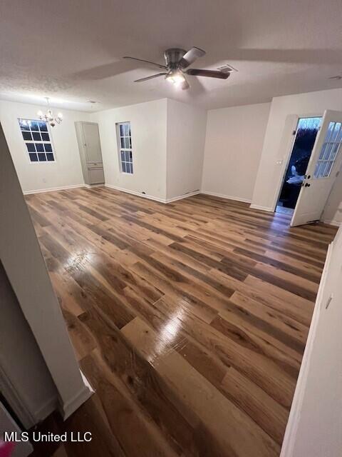 empty room featuring wood finished floors, ceiling fan with notable chandelier, and baseboards
