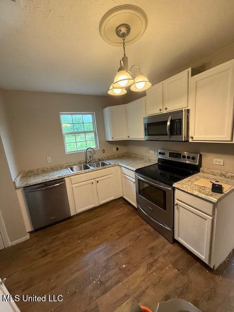 kitchen with dark wood-style floors, a sink, pendant lighting, white cabinets, and appliances with stainless steel finishes