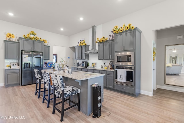 kitchen featuring gray cabinetry, stainless steel appliances, wall chimney range hood, and a kitchen island with sink