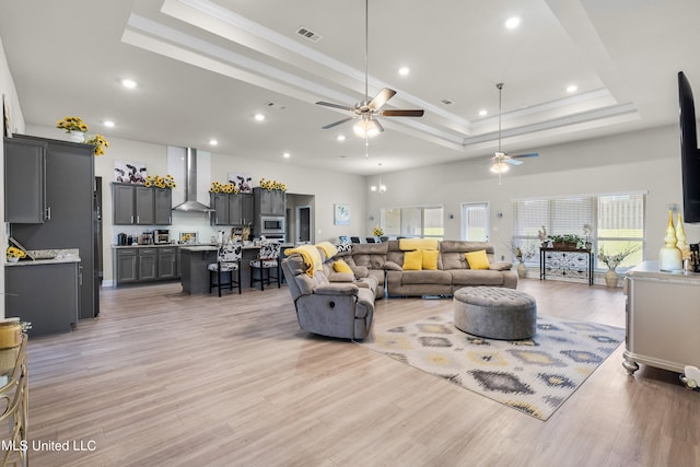 living room featuring ornamental molding, a tray ceiling, light wood-type flooring, and ceiling fan