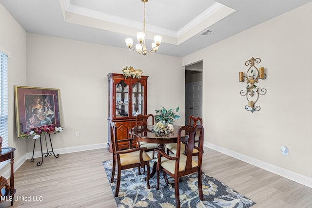 dining room with an inviting chandelier, ornamental molding, a tray ceiling, and light hardwood / wood-style floors