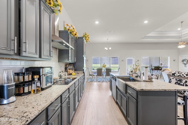 kitchen with wall chimney range hood, an island with sink, a kitchen bar, gray cabinets, and sink