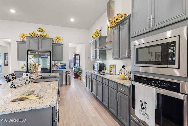 kitchen with decorative backsplash, stainless steel appliances, light stone countertops, light wood-type flooring, and gray cabinets