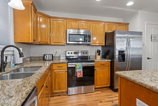 kitchen featuring appliances with stainless steel finishes, light wood-type flooring, light stone counters, and sink