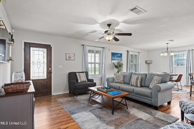 living room featuring ceiling fan with notable chandelier, a healthy amount of sunlight, and dark hardwood / wood-style flooring