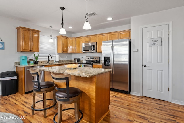 kitchen featuring stainless steel appliances, sink, a center island, light hardwood / wood-style flooring, and hanging light fixtures