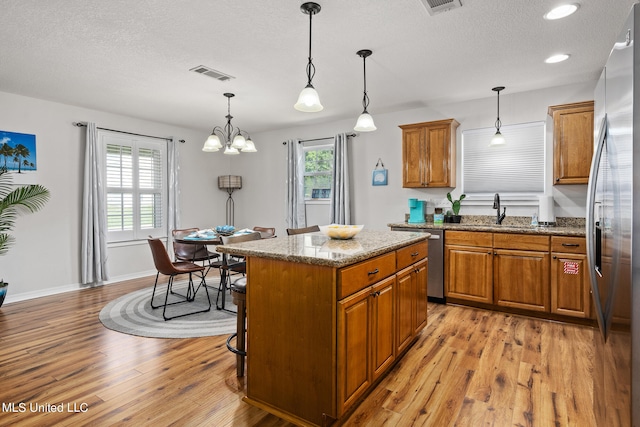 kitchen featuring stainless steel appliances, hanging light fixtures, a center island, light stone countertops, and sink