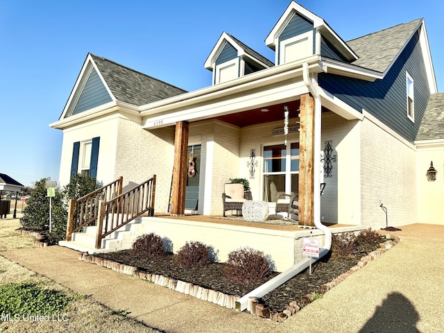 view of front of house with brick siding, covered porch, and roof with shingles