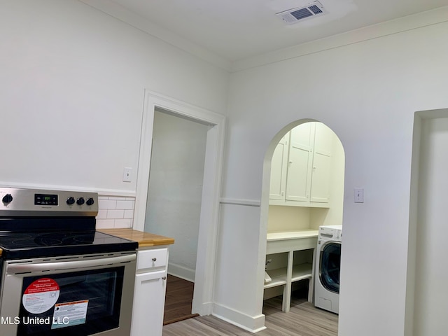 kitchen featuring washer / dryer, backsplash, stainless steel range with electric stovetop, white cabinets, and light hardwood / wood-style flooring