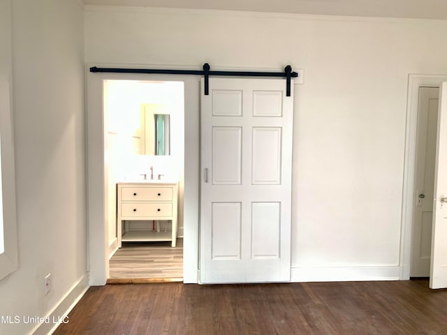 unfurnished bedroom with dark hardwood / wood-style floors, a closet, ornamental molding, sink, and a barn door