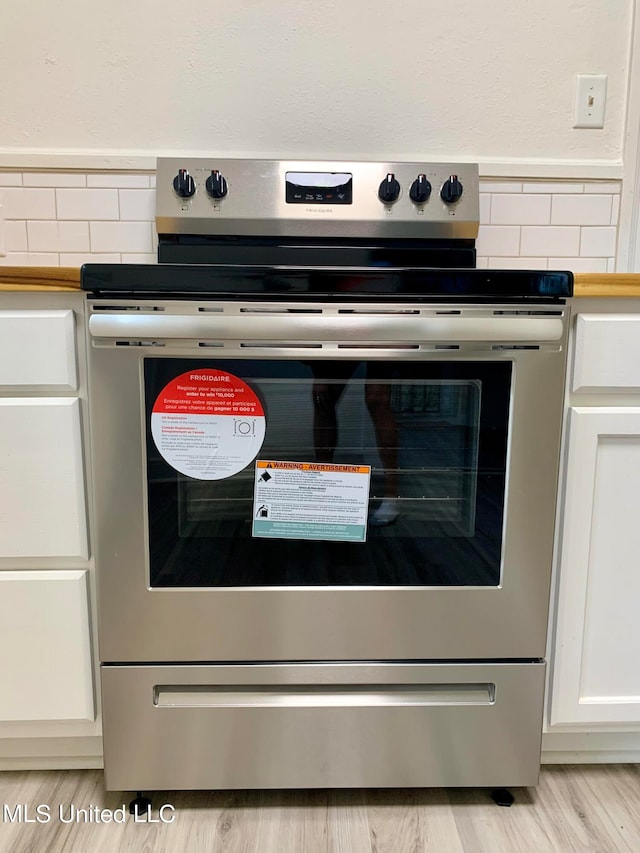 room details featuring decorative backsplash, light hardwood / wood-style floors, white cabinetry, and stainless steel stove