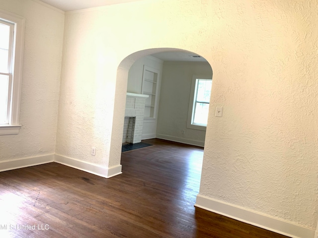 unfurnished room with dark wood-type flooring and a brick fireplace