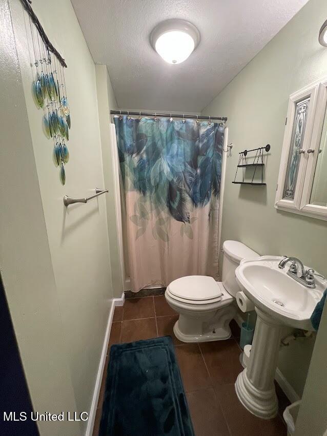 bathroom featuring a shower with curtain, sink, tile patterned flooring, toilet, and a textured ceiling