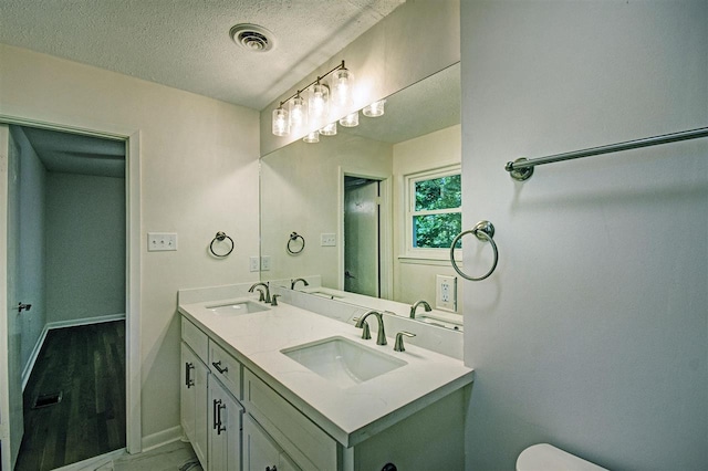 bathroom featuring double vanity, visible vents, a textured ceiling, and a sink