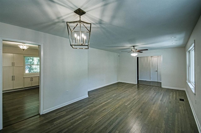 empty room featuring visible vents, ceiling fan with notable chandelier, baseboards, and dark wood-style flooring