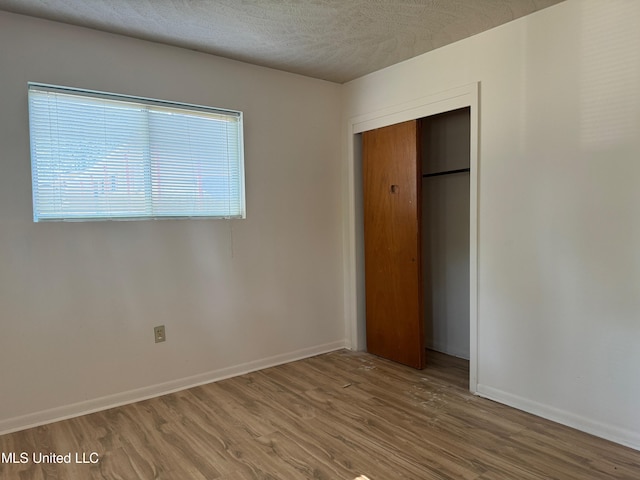 unfurnished bedroom with a textured ceiling, a closet, baseboards, and wood finished floors