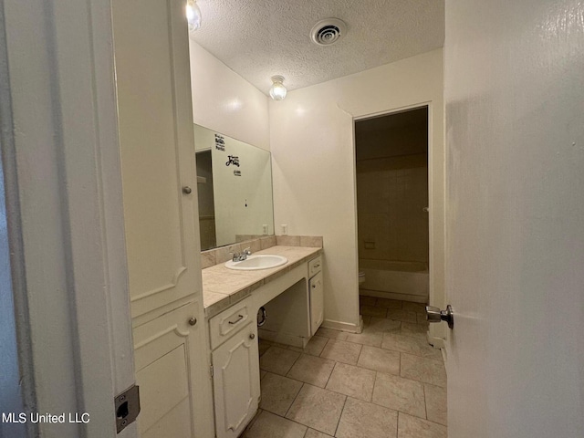 bathroom with a textured ceiling, toilet, vanity, and visible vents