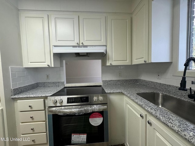 kitchen with tasteful backsplash, white cabinetry, a sink, under cabinet range hood, and stainless steel electric range