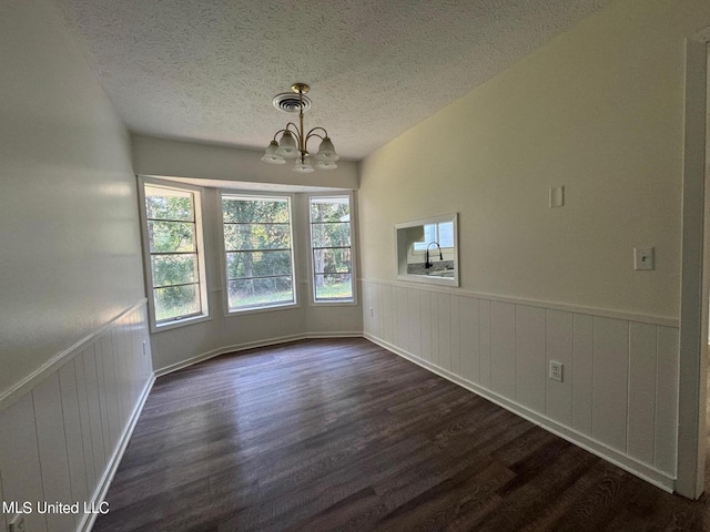 interior space featuring a textured ceiling, a notable chandelier, a wainscoted wall, visible vents, and dark wood finished floors