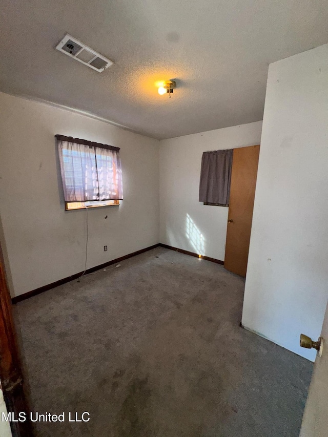 carpeted spare room with visible vents and a textured ceiling