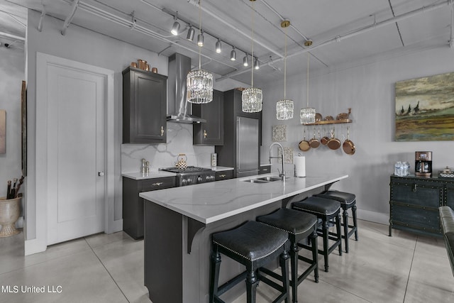 kitchen with wall chimney range hood, sink, an island with sink, a kitchen breakfast bar, and hanging light fixtures