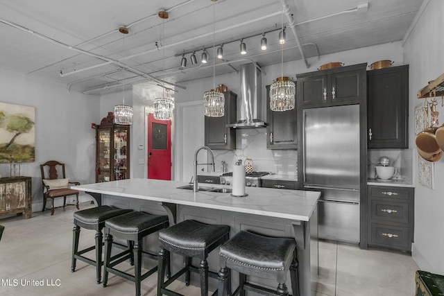 kitchen with a large island with sink, appliances with stainless steel finishes, a kitchen breakfast bar, wall chimney exhaust hood, and decorative light fixtures