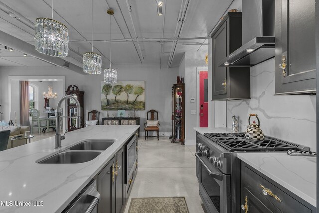 kitchen with light stone countertops, wall chimney range hood, sink, appliances with stainless steel finishes, and hanging light fixtures