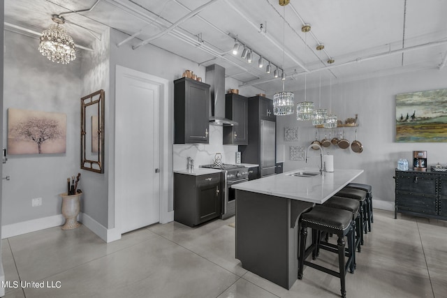 kitchen featuring wall chimney range hood, sink, high end range, pendant lighting, and a kitchen island with sink