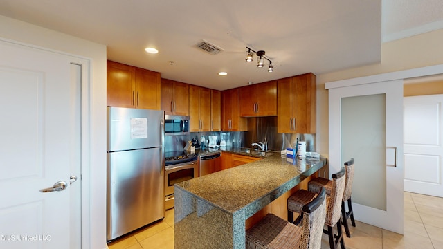 kitchen with a breakfast bar area, kitchen peninsula, light tile patterned flooring, and stainless steel appliances