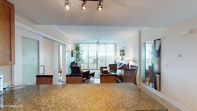 interior space featuring a textured ceiling, rail lighting, ceiling fan, and dark stone countertops