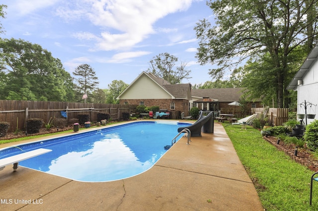 view of swimming pool with a diving board, a fenced backyard, a patio, and a water slide