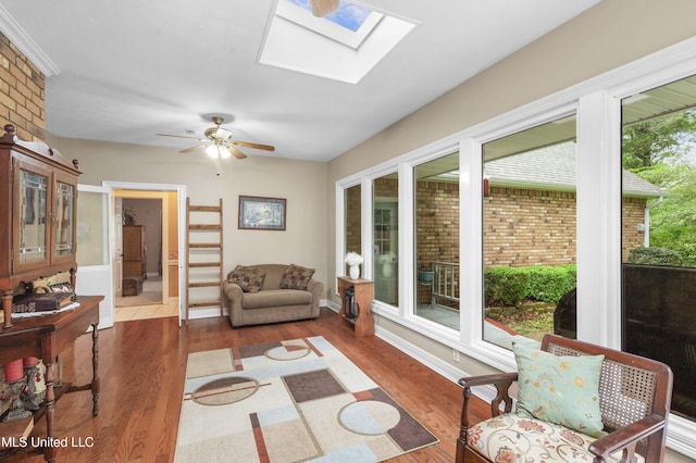 living area with a skylight, wood finished floors, a ceiling fan, and baseboards
