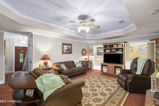 living area featuring a tray ceiling, wood finished floors, crown molding, ceiling fan, and baseboards
