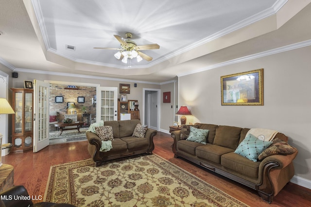 living room featuring a tray ceiling, wood finished floors, ceiling fan, crown molding, and baseboards