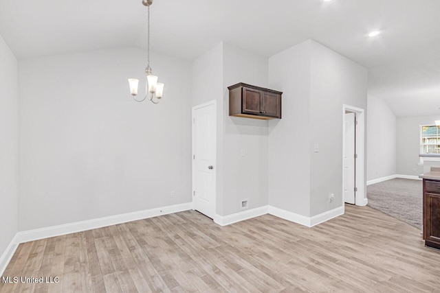 spare room with light wood-type flooring, vaulted ceiling, and an inviting chandelier