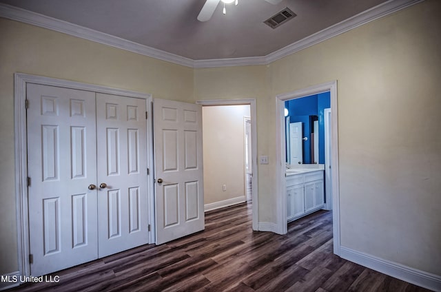 unfurnished bedroom with ensuite bathroom, a closet, ceiling fan, dark wood-type flooring, and crown molding