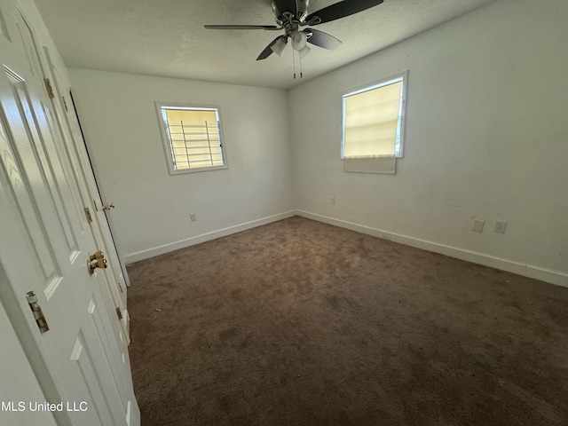 unfurnished room with ceiling fan, a healthy amount of sunlight, and dark colored carpet