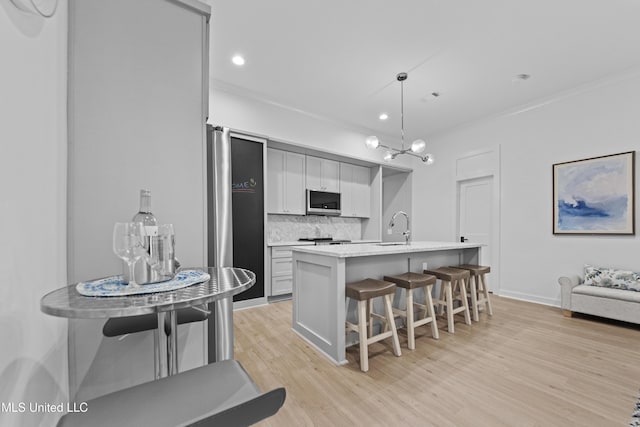 kitchen with appliances with stainless steel finishes, a sink, ornamental molding, tasteful backsplash, and a breakfast bar area