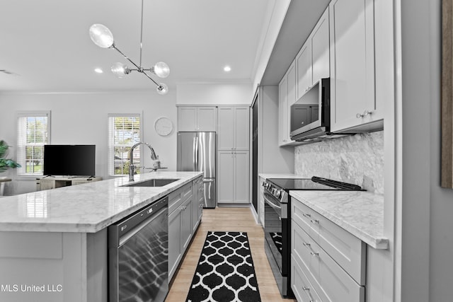 kitchen with stainless steel appliances, a sink, gray cabinetry, light wood finished floors, and a center island with sink