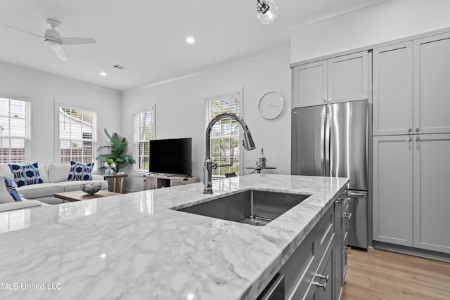 kitchen featuring a sink, crown molding, light stone counters, light wood-style flooring, and freestanding refrigerator