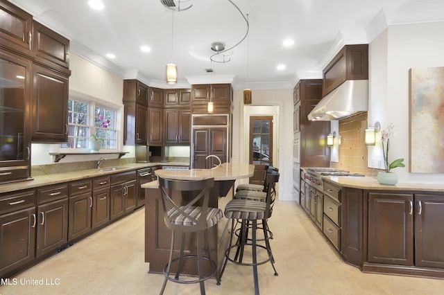 kitchen with stainless steel gas stovetop, a kitchen island with sink, wall chimney exhaust hood, decorative backsplash, and dark brown cabinetry