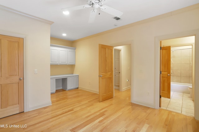 unfurnished bedroom with ceiling fan, crown molding, ensuite bathroom, light hardwood / wood-style floors, and built in desk